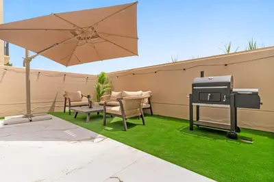 a barbecue grill on a lawn with chairs and an umbrella at 3BR Luxury Townhouse with Garden in Dubai