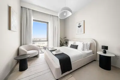 a white bedroom with a large bed and a chair at VayK - Classy 1BR Near the Lagoon in Creek Harbour in Dubai