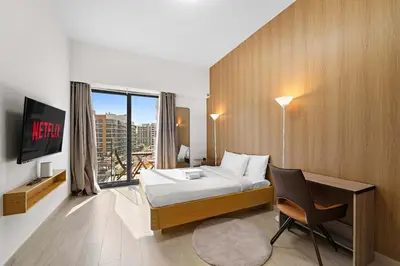 a bedroom with a bed and a desk and a window at Charming Studio with Pool, Gym, Kid's playground in Dubai