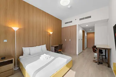 a bedroom with a large white bed and a desk at Charming Studio with Pool, Gym, Kid's playground in Dubai