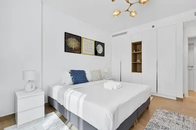 a white bedroom with a large bed and a chandelier at Stylish 1BR Port De La Mer Escape with Beach Access in Dubai