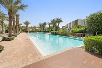 a swimming pool with palm trees and a building at Spacious 4BR Villa with Private Garden & Patio in Nadd Shubayḩ