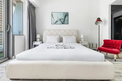a white bedroom with a large white bed and a red chair at 1BR at Ocean Heights Next to Tram Station in Dubai