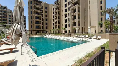 a swimming pool in a building with chairs and an umbrella at StayShort - MJL Apartment for 2 people near Water Parks in Dubai