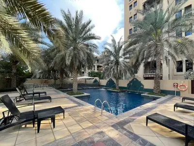 a pool with benches and palm trees next to a building at Dubai 2BR Pool View, Near Burj Khalifa, Canal & Attractions in Dubai
