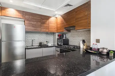 a kitchen with wooden cabinets and a stainless steel refrigerator at Lush 1BR Oasis in JVC With Gym & 5min to Circle Mall in Dubai