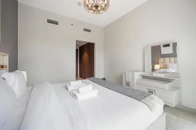 a white bedroom with a large bed and a sink at Lush 1BR Oasis in JVC With Gym & 5min to Circle Mall in Dubai