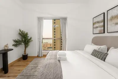 a white bedroom with a large bed and a window at 4 Bedroom Sea View Apartment in Jumeirah Beach Residence in Dubai