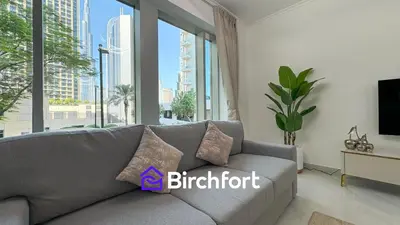 a living room with a gray couch and a large window at Birchfort- Downtown Living with Burj Khalifa View in Dubai
