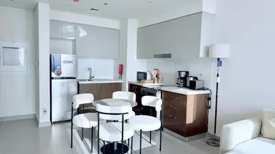 a kitchen with white appliances and white stools at Elegant Downtown Escape 1BR w Balcony, Pool & Gym in Dubai