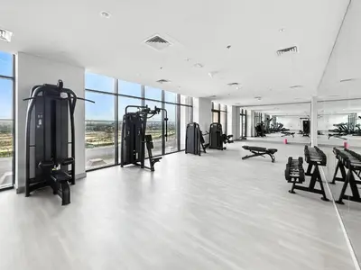 a gym with treadmills and machines in a room with windows at 1BR Azizi Riviera 44 City Skyline View in Dubai