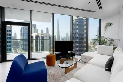 a living room with a white couch and blue chairs at Maison Privee - Sky-High Panoramic Apt with Iconic Burj Khalifa Vws in Dubai