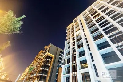 a tall white building with a palm tree in front of it at Cozy Apartments in Azizi Riviera Dubai in Dubai