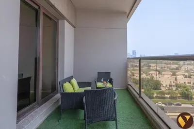 a balcony with a couch and chairs and a large window at Vogue Sports City Elite near First Avenue Mall, One Bedroom Apartment with Balcony and Vibrant Community View, Access to all Amenities in Dubai