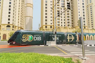 a green train on a city street with tall buildings at Modern 2BR Apartment at JBR in Dubai