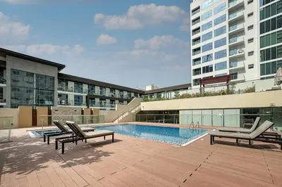 a swimming pool with lounge chairs and a building at Bright and Stylish 2 Bed Home Opposite Circle Mall in Dubai