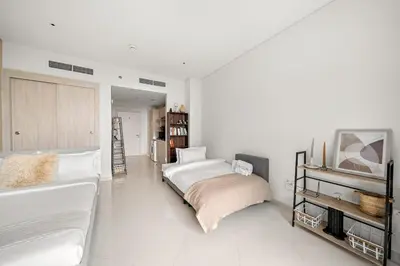 a white bedroom with a bed and a tv at FIRST CLASS Studio Infinity Pool and Luxe Vibes in Dubai