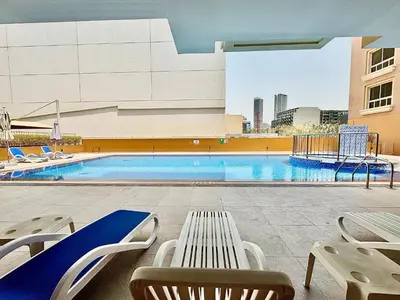 a swimming pool with two chairs and a table and a building at Homes2Retreat - JVC Charm - 1BR Apt with Private Balcony in Dubai
