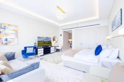 a white bedroom with a large bed and a blue chair at Scenic Studio at Palm Tower in Dubai