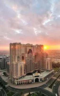 a large building with a sunset in the background at Lovely Studio with balcony in Silicon Oasis in Dubai