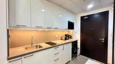 a kitchen with white cabinets and a sink and a black door at Lovely Studio with balcony in Silicon Oasis in Dubai
