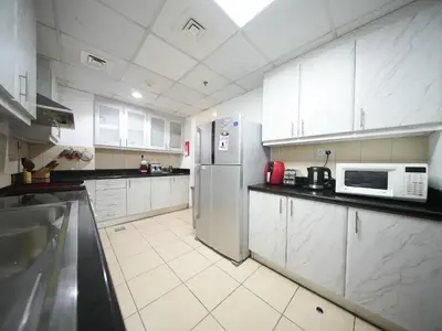a kitchen with white cabinets and a stainless steel refrigerator at Happyland JBR Dubai Hostel in Dubai