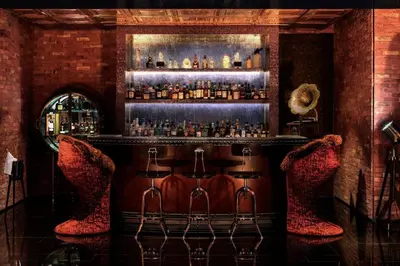 a bar with two red chairs and a shelf with liquor bottles at 2BR Apartment in Paramount Hotel with Burj Khalifa View in Dubai
