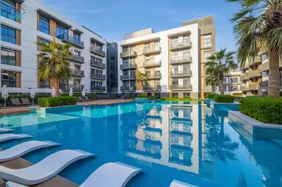 a swimming pool with lounge chairs in front of a building at Contemporary 2-BR at Belgravia Square JVC in Dubai