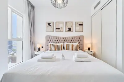 a white bedroom with a large white bed with pillows at Chic & Modern 1BR in Socio Near Dubai Hills Park in Dubai