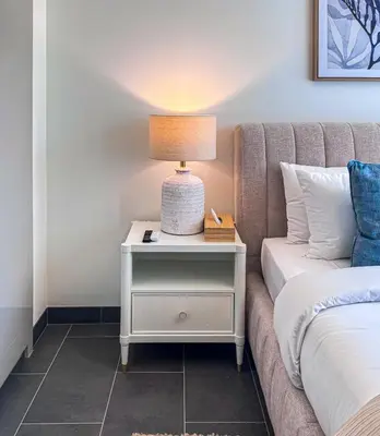 a bedside table with a lamp on it next to a bed at Luxury 1BR, The Crest, Sobha Hartland in Dubai
