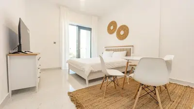 a white bedroom with a bed and a table and chairs at Cozy Studio in JVC in Dubai