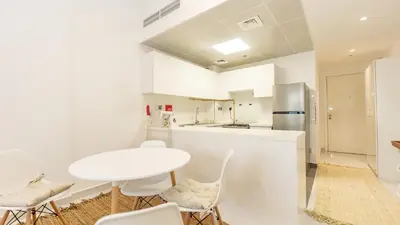 a white kitchen with a white table and chairs at Cozy Studio in JVC in Dubai