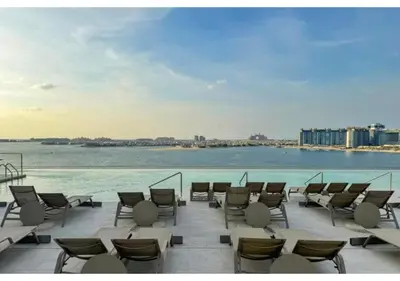 a row of chairs and tables on a patio next to the water at KeyRock - Palm View Apt with Pool & Gym Access in Dubai