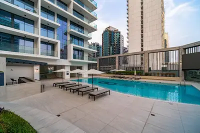 a pool with chairs and umbrellas next to a building at SettlerHomes - Lux 20F Stay With Gym, Pool & Cinema in Dubai