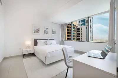 a white bedroom with a bed and a desk with a laptop at Sea & City View Apartment Dubai Marina - Ravello Living in Dubai