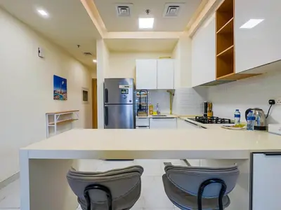 a kitchen with a white counter and two stools at Comfortable Studio Living in Dar Al Jawhara, JVC in Dubai
