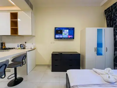 a kitchen with a bed and a desk and a tv on the wall at Comfortable Studio Living in Dar Al Jawhara, JVC in Dubai