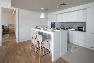 a kitchen with white cabinets and a bar with stools at Frank Porter - Bluewaters Residences 5 in Dubai