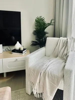 a living room with a white chair and a tv at Soft Toned 1BR Retreat with Pool, Gym and Parking! in Dubai