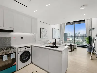 a white kitchen with a washing machine and a living room at Chic and Stylish 1 BDR in Binghatti corner - JVC in Dubai