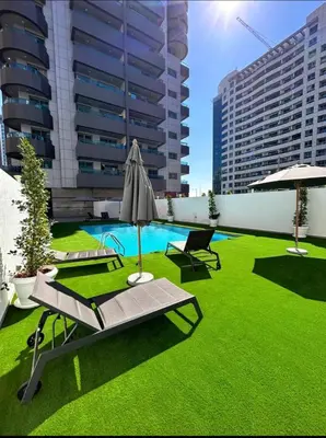 a patio with grass and an umbrella and a pool at The S Royal Marina Boutique Stay For Ladies And Families Only in Dubai