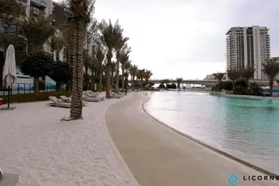 a swimming pool with palm trees next to a building at Brand New Modern 2 BR Retreat in Dubai Creek Harbour in Dubai