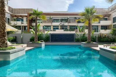 a swimming pool in front of a building with palm trees at Oxford Boulevard - Vibrant Studio in JVC in Dubai