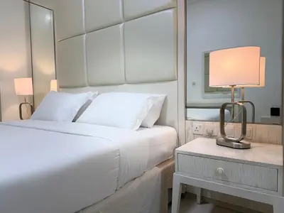 a white bedroom with a bed and a table with a lamp at ASHRI Luxury apt Steps to Dubai Mall & Burj Khalifa in Dubai