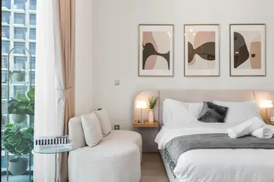 a white bedroom with two beds and a chair at Sleek Cozy Apartments in Meydan in Dubai