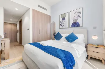 a bedroom with a large white bed with blue accents at Cozy Luxe Studios in Meydan in Dubai
