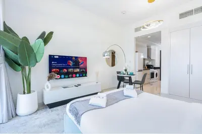 a white living room with a tv on a wall at PVH - Serene Studio with Skyline View - Carson B in Dubai