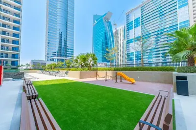 a park with benches and a playground with tall buildings at KeyRock - Modern 1BR in Zada with Pool & View in Dubai