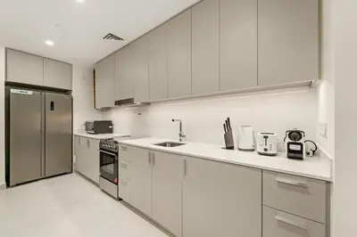 a kitchen with white cabinets and a stainless steel refrigerator at Prime 2BR Retreat, Creek Harbour Views & Comfort Near Restaurants in Dubai