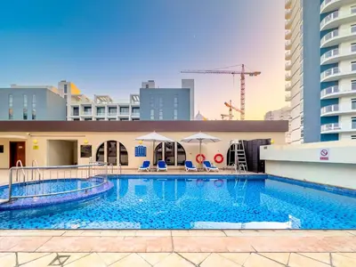 a pool with chairs and umbrellas next to a building at Dubai 1BR Balcony Views Near Miracle Garden in Dubai